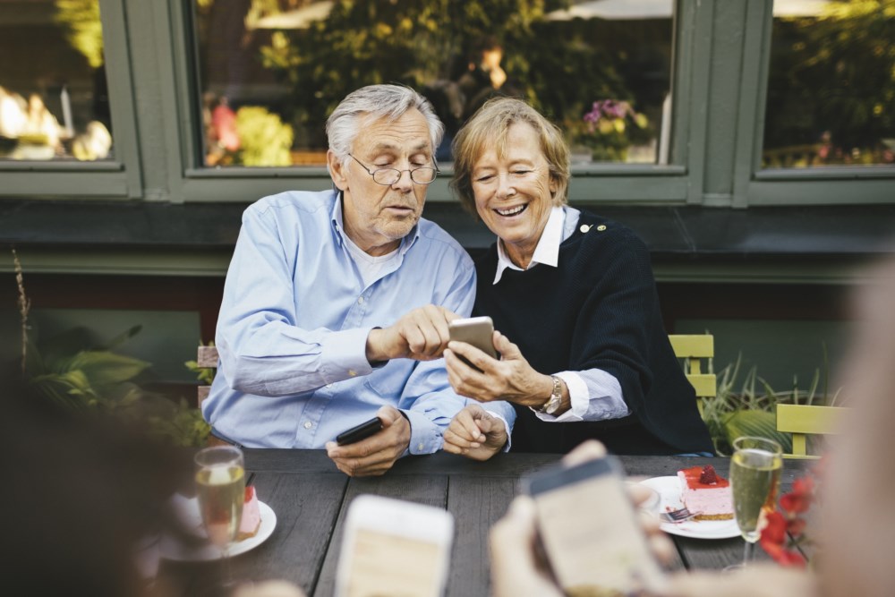 Mann og dame sitter ute og ser på mobilen
